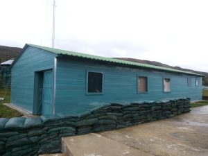 Campamento modular Maderplast en polipropileno color azul, instalado en base militar sobre plataforma de concreto, con sacos de protección perimetral.