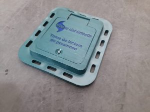Tapa en polipropileno para cajilla de medidor domiciliario de agua, con logo personalizado y sistema de cierre seguro instalada sobre superficie de concreto.